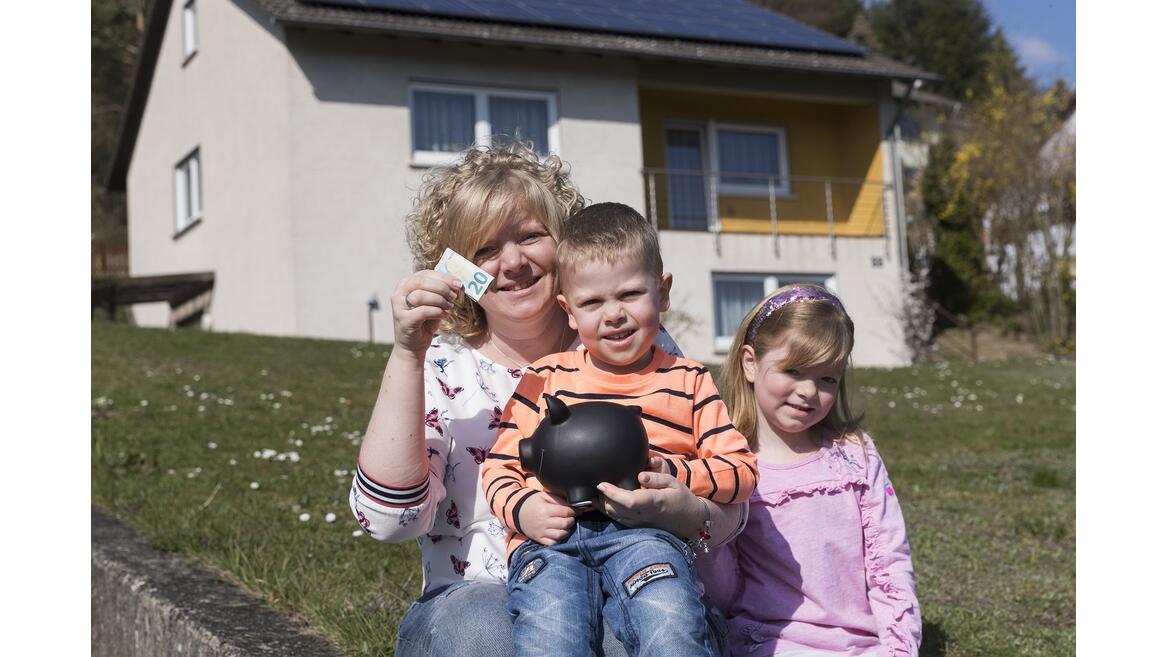 Familie Gasner mit Sparschwein vor dem Haus