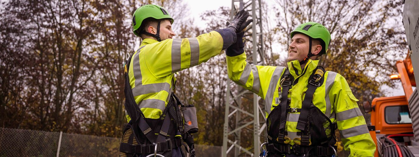 Zwei Kollegen draußen, in Kletterausrüstung klatschen sich lachend ab
