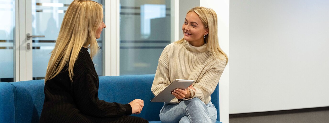 Zwei weibliche Studierende im Gespräch und auf dem Sofa sitzend