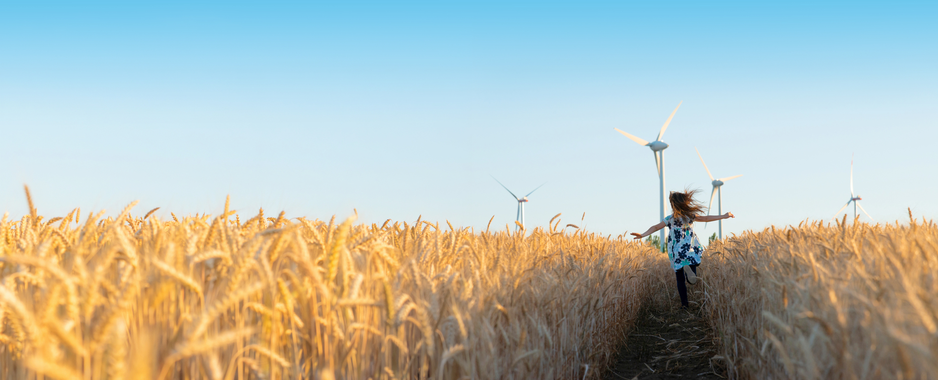 Frau rennt durch Kornfeld mit Windrädern im Hintergrund