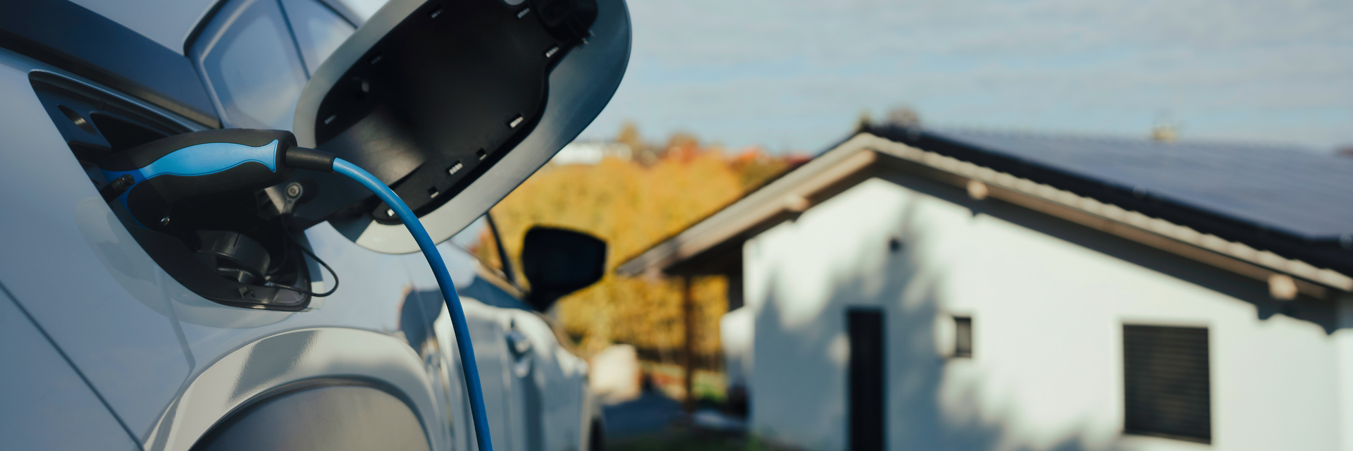 Elektroauto am Ladekabel angeschlossen, im Hintergund ein Haus mit Solaranlage auf dem Dach