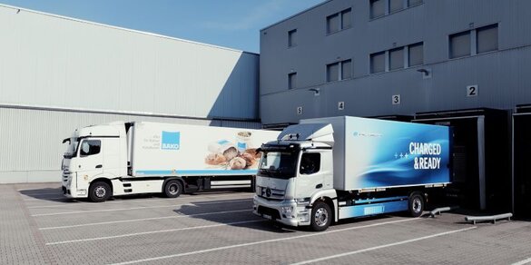 Zwei LKW stehen stehen vor einem Gebäude und werden beladen.
