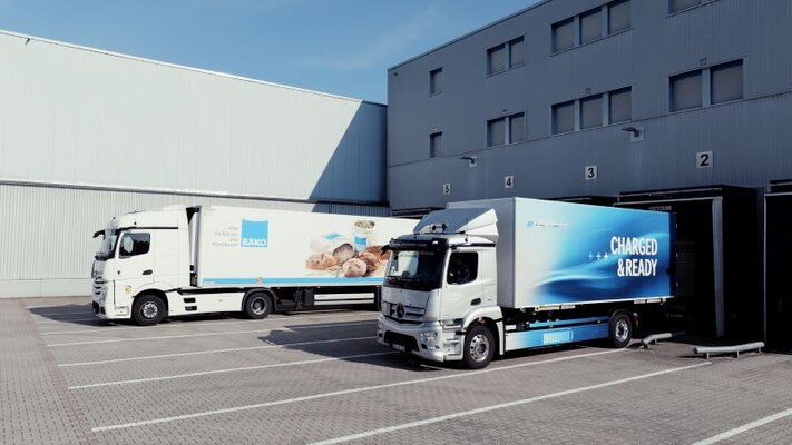 Zwei LKW stehen vor einem Gebäude und werden beladen. 