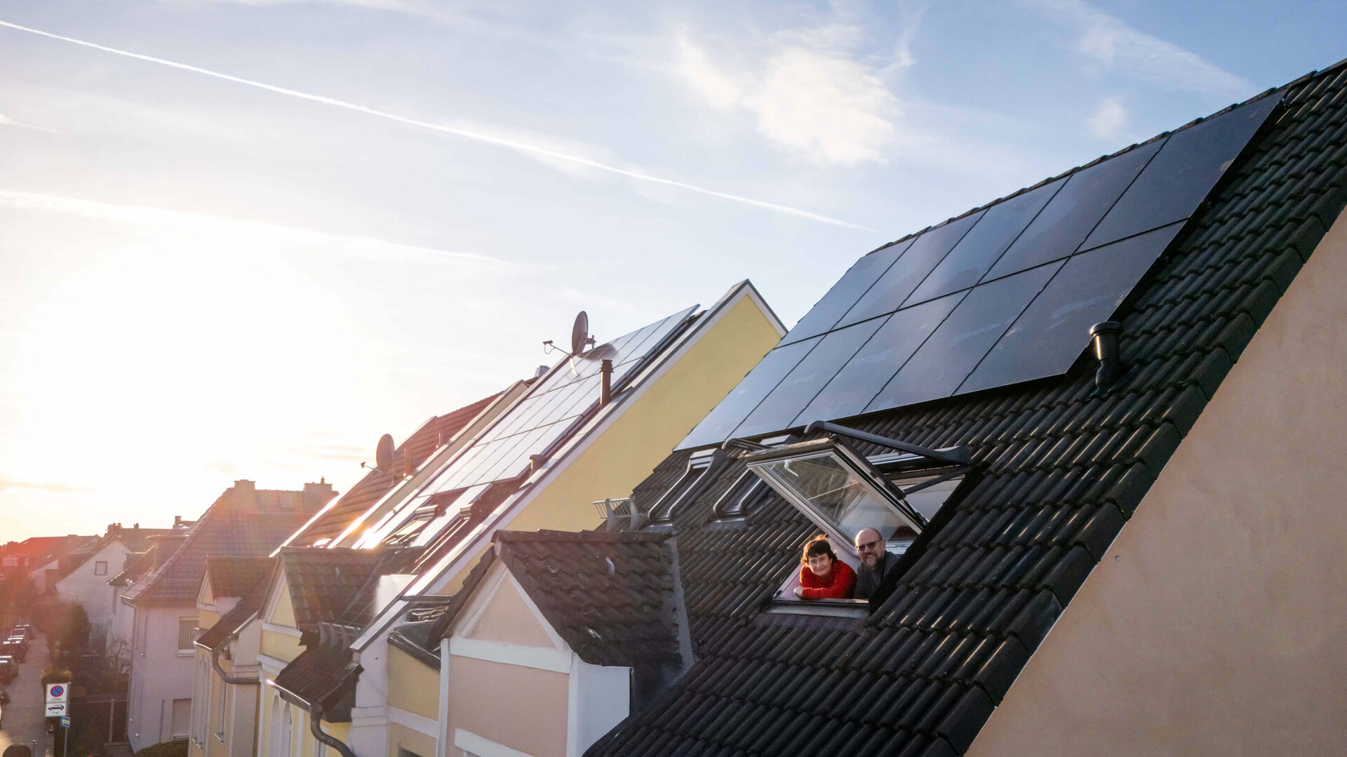 Paar schaut aus dem Dachfenster, umgeben von der Solaranlage  | © Bildnachweis: © Pfalzwerke/Marc Wilhelm