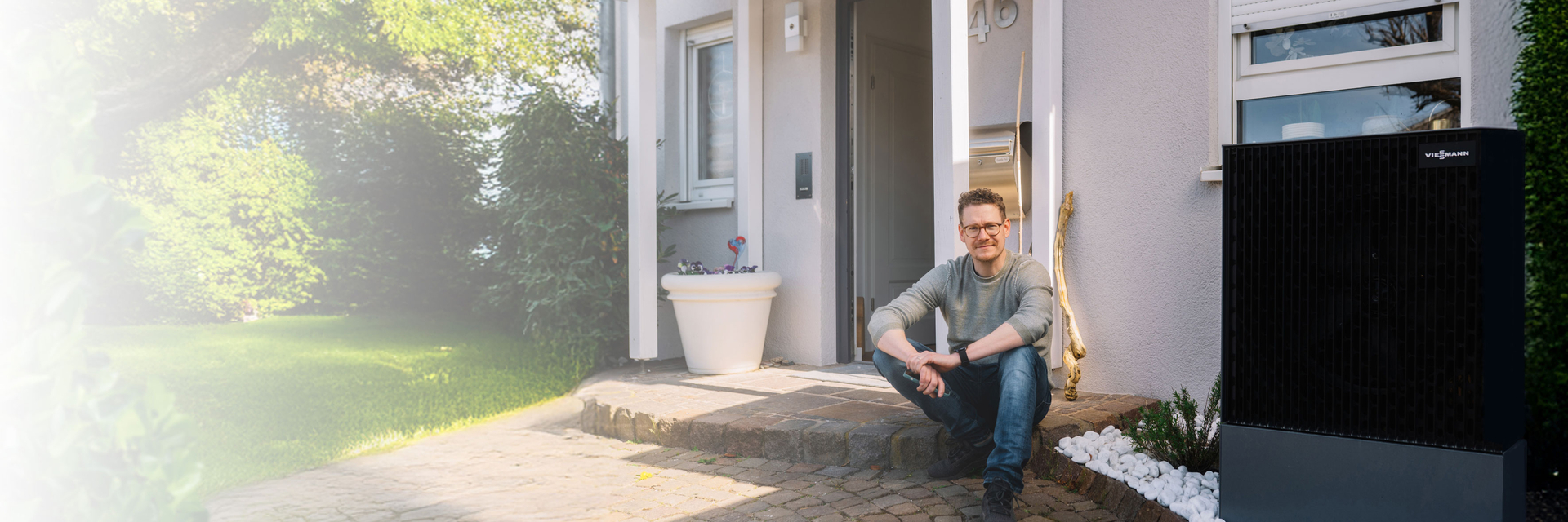 Junger Mann sitzt vor seinem Haus mit einer Wärmepumpe | © Bildnachweis: © Pfalzwerke/Patrick Junker
