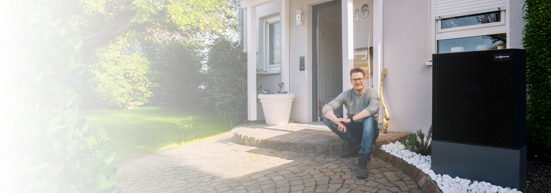 Junger Mann sitzt vor seinem Haus mit einer Wärmepumpe | © Bildnachweis: © Pfalzwerke/Patrick Junker