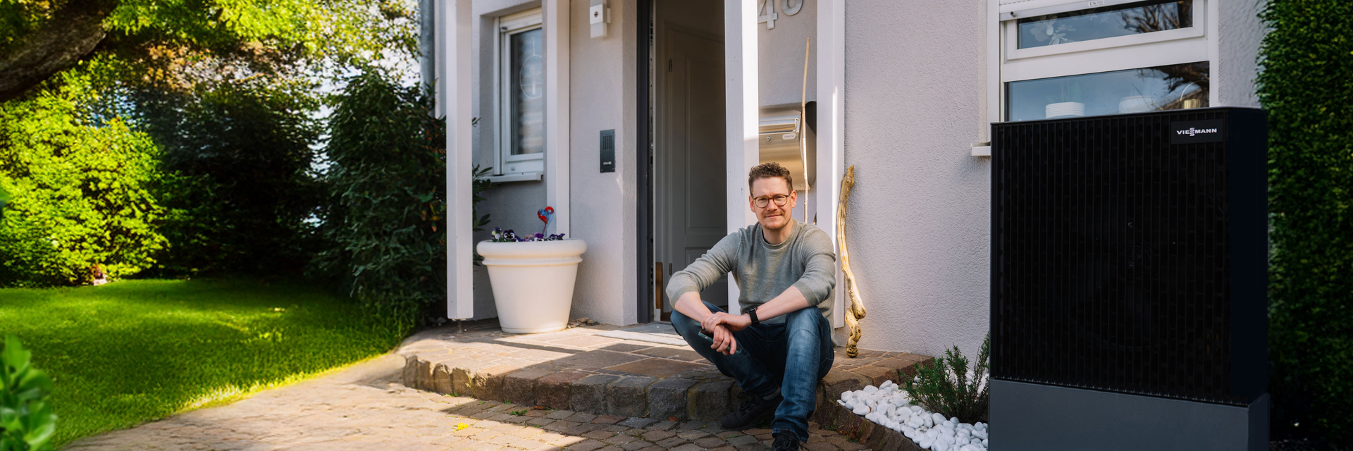 Junger Mann sitzt vor seinem Haus mit einer Wärmepumpe | © Bildnachweis: © Pfalzwerke/Patrick Junker