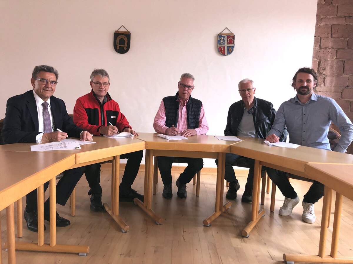 Fünf Männer sitzen am Tisch und unterzeichnen Dokumente.