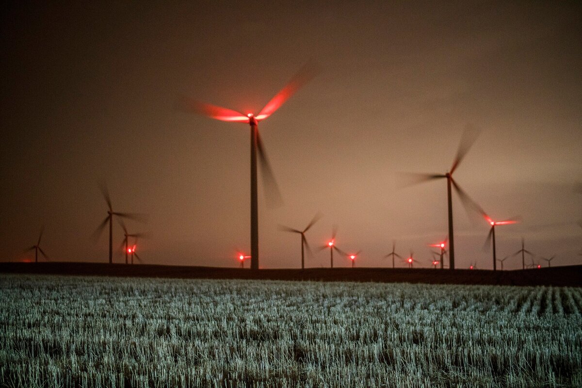 Beleuchtete Windräder drehen sich in der Nacht. 