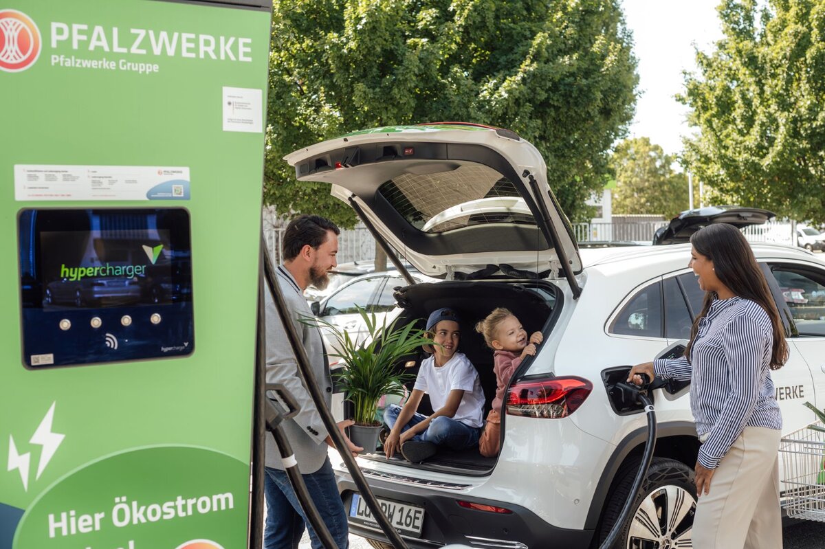 Eine Familie lädt ihr E-Auto an einer Ladesäule. Die Kinder sitzen im Kofferraum, die Eltern stehen neben dem Auto. 