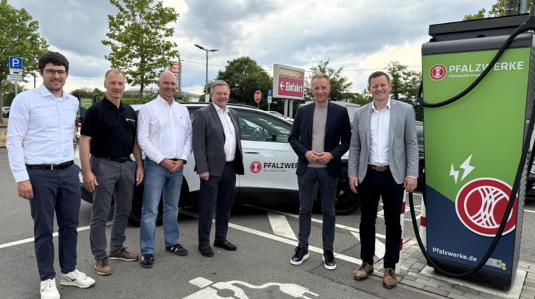Mehrere Personen stehen an einem Pfalzwerke-Elektrofahrzeug neben einer E-Ladesäule auf dem Parkplatz eines Hornbach-Markts.